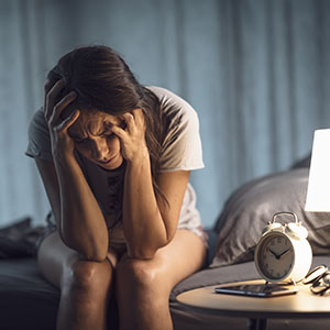 Woman with hands on head, sitting on a bed next to an alarm clock, SSDI claim in Florida.